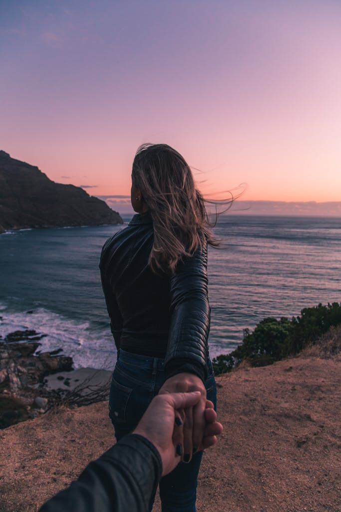Woman holding mans hand looking out on the ocean with mountians in the background of an award travel